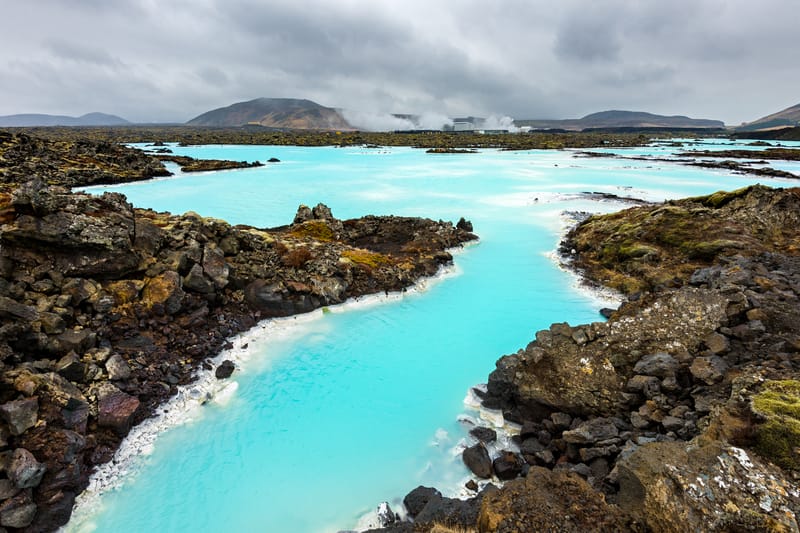 Empty milky-blue geothermal waters of the Blue Lagoon in Iceland, surrounded by dark volcanic rocks and steam rising gently