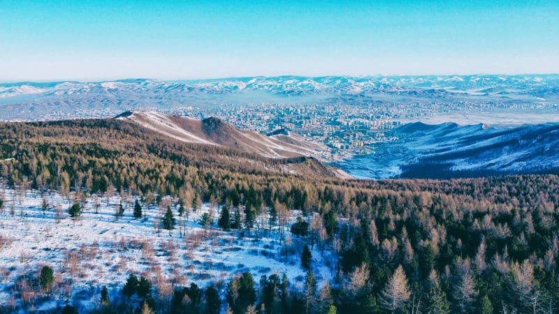 A wintry aerial view of Ulaanbaatar surrounded by snow-dusted mountains, when Mongolia is least expensive for tourists