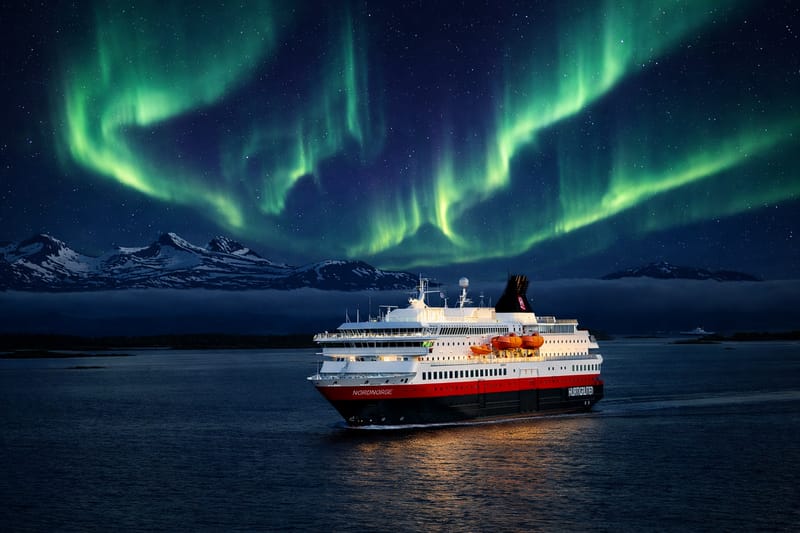 The Hurtigruten coastal express sails beneath the Northern Lights on its iconic route along the Norwegian coast.