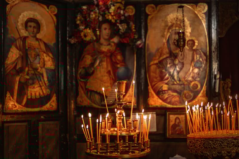Votive candles burn before gilded icons inside an Orthodox church, a scene familiar to Christian pilgrimage groups travelling through Greece, Eastern Europe, and the Holy Lands.