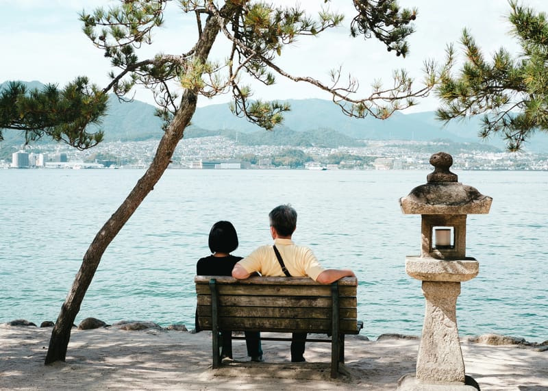A couple sits by the waterfront on Miyajima Island, looking out across the Seto Inland Sea