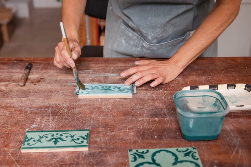 Portuguese artist painting a ceramic tile using traditional azulejo techniques.