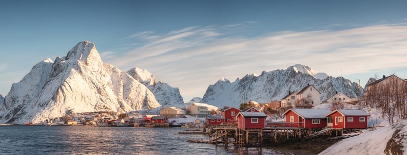 Traditional red and yellow rorbu fishing huts line the coastline of the Lofoten Islands, reflected in the still Arctic waters.