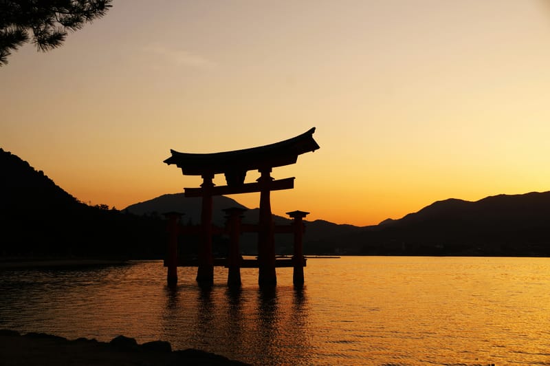 Sunset at Itsukushima Shrine on Miyajima Island, with the torii gate silhouetted against the sky